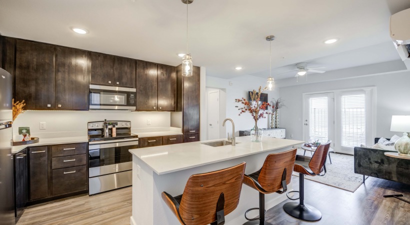 Luxury kitchen at FLATZ 520 features dark cabinets, stainless appliances, island with stools, and adjacent living area.